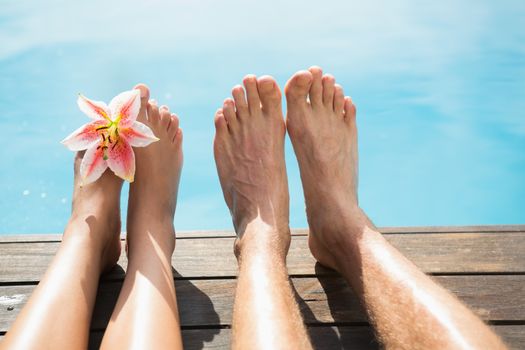 Close up of couples bare feet against swimming pool on a sunny day