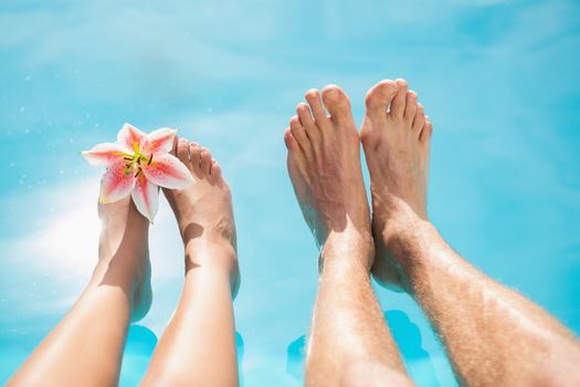 Close up of couples bare feet against swimming pool on a sunny day