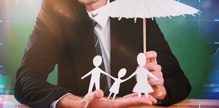 Businessman holding umbrella and paper family against green chalkboard