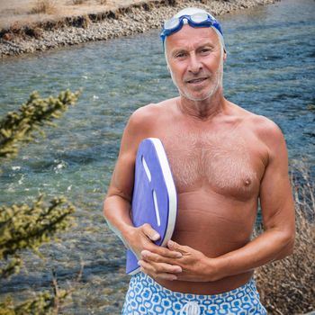 Portrait of senior male swimmer with swimming float against flowing river in forest