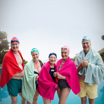 Portrait of senior friends in swimwear covered with towels against swimming pool against clear sky