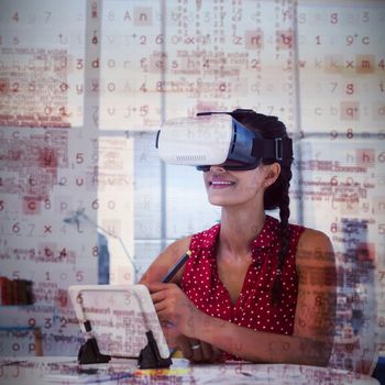 Female graphic designer in virtual reality headset using digital tablet at desk in office