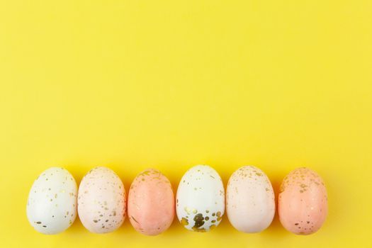 Creatively painted eggs in pastel colors decorated with gold leaf are arranged in row along bottom edge on yellow background, copy space. Happy Easter DIY concept. Flat lay. Horizontal.