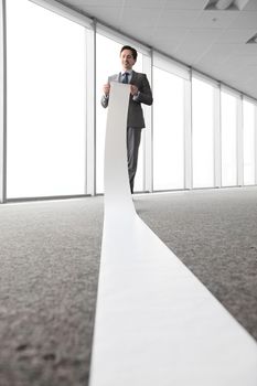 Business man reading a long paper band roll in office