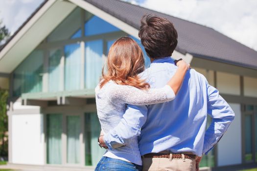 Happy couple stand outdoors hug and look at their new house