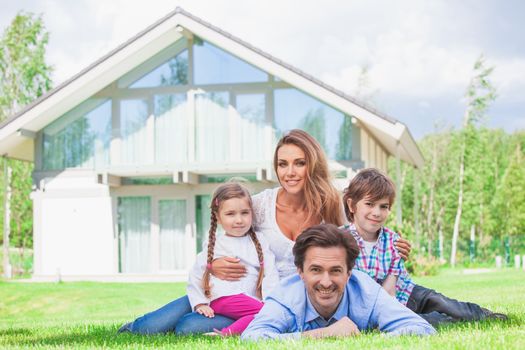 Family of four people laying on grass in front of house