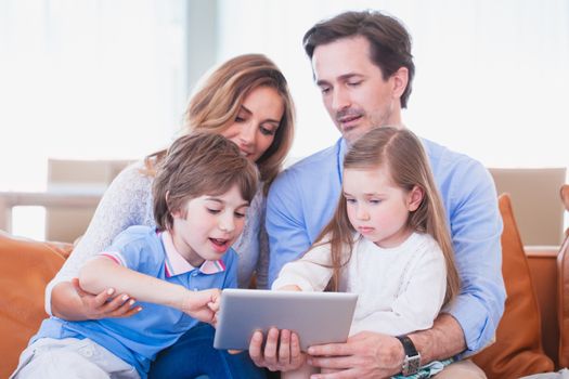Portrait of happy family with two children sitting on sofa with tablet pc
