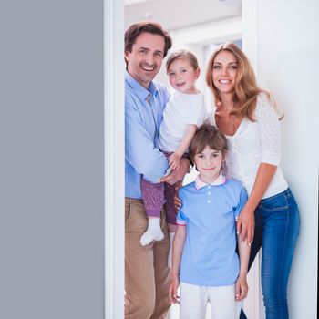 Cheerful family of parents and two children inviting to enter in home standing in doorway