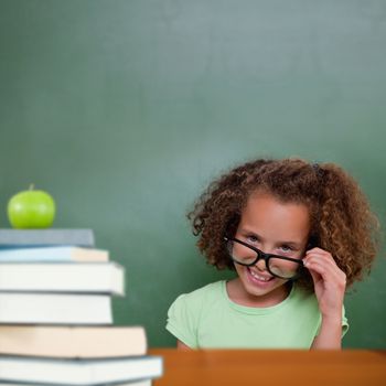 Cute pupil tilting glasses against green apple on pile of books