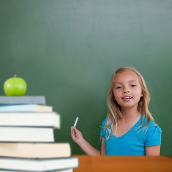Green apple on pile of books against cute pupil holding chalk