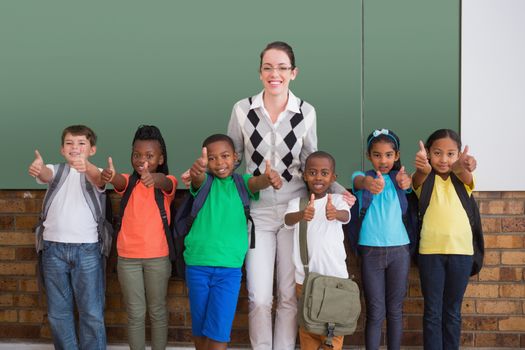 Cute pupils smiling at camera in classroom showing thumbs up at the elementary school