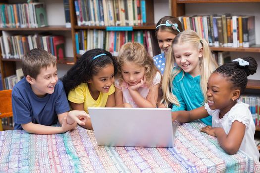 Cute pupils looking at laptop in library at the elementary school