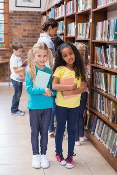 Cute pupils and teacher looking for books in library at the elementary school