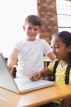 Cute little pupils looking at laptop in classroom at the elementary school