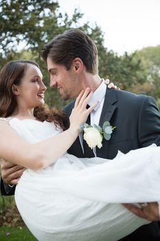 Romantic bridegroom carrying bride while standing in park