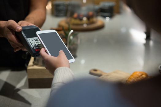 Woman paying bill through smartphone using NFC technology in restaurant