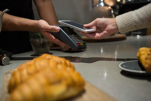 Woman paying bill through smartphone using NFC technology in restaurant