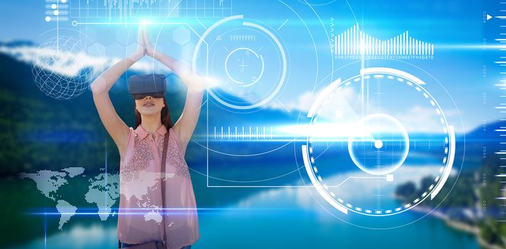 Young woman with arms raised looking through virtual reality simulator against blue technology interface with glow