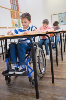 Disabled pupil writing at desk in classroom at the elementary school