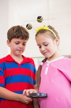 Cute pupils looking through magnifying glass at the elementary school