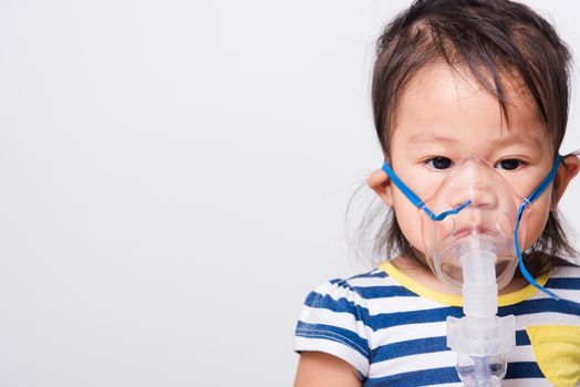 Closeup Asian face, Little baby girl sick her using steam inhaler nebulizer mask inhalation oneself on white background with copy space, health medical care