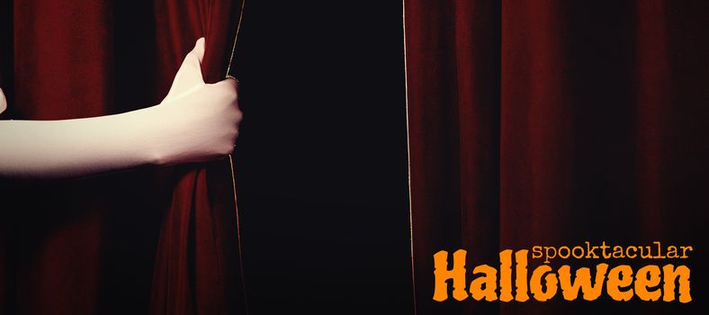 Graphic image of spooktacular Halloween text against cropped hand holding curtain at stage