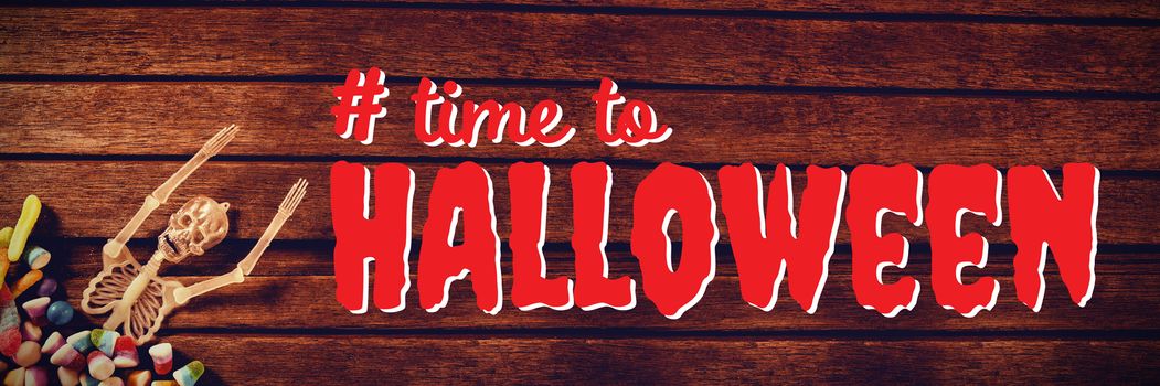 Digital composite image of time to Halloween text against skeleton decoration with candies on wooden table