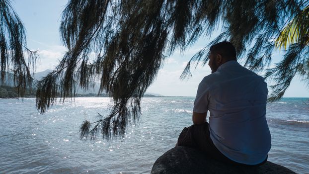 Along man sitting on a rock relaxing and reflexion with a beautiful blue sky and sea