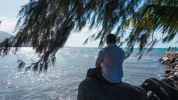 Along man sitting on a rock relaxing and reflexion with a beautiful blue sky and sea