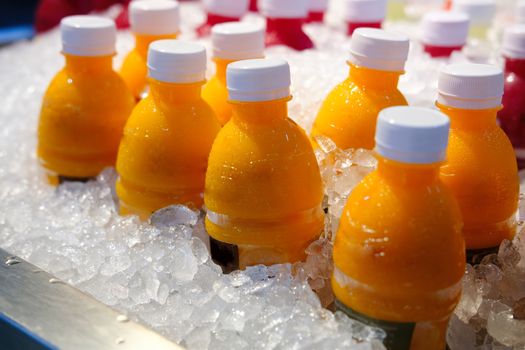 Homemade Fresh Orange juice bottles on the ice box. Mix of plastic bottles on the ice bucket for sale in Thailand food market. 