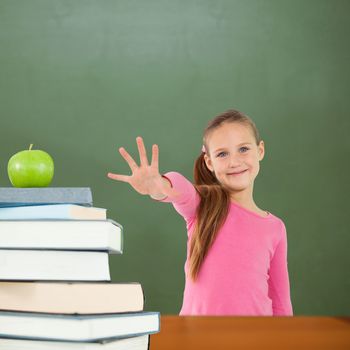 Cute girl with hand out against green apple on pile of books in classroom