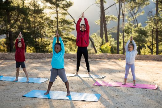 Coach assisting kids in practicing yoga on a sunny day