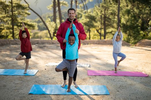 Coach assisting kids in practicing yoga on a sunny day