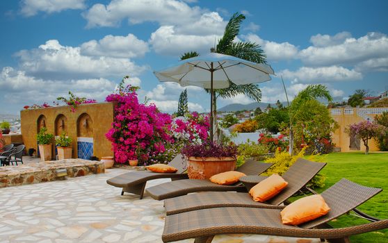 Brown wicker chaise lounges on a stone patio with orange cushions