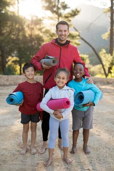 Portrait of coach and kids standing with yoga mat in park