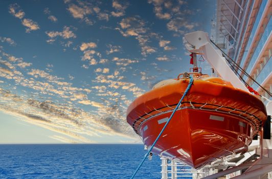 An orange lifeboat hanging over a blue sea on the side of a cruise ship