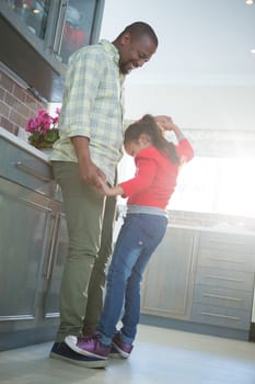 Smiling father and daughter dancing together in kitchen