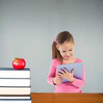 Cute girl using tablet against red apple on pile of books in classroom