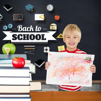 Cute boy showing his art against green apple on pile of books in classroom