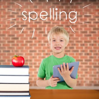 The word spelling and cute boy using tablet against red apple on pile of books
