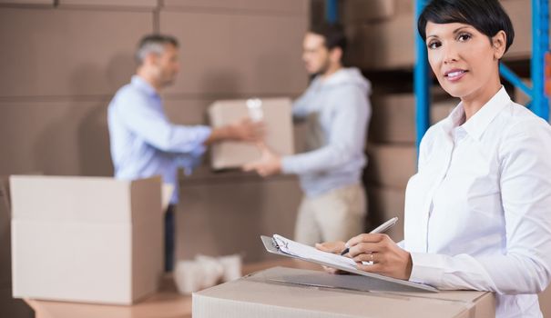 Warehouse manager writing on clipboard in a large warehouse