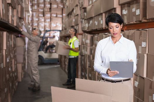 Pretty warehouse manager writing on clipboard in a large warehouse