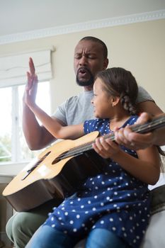 Father teaching his daughter to play the guitar in bedroom