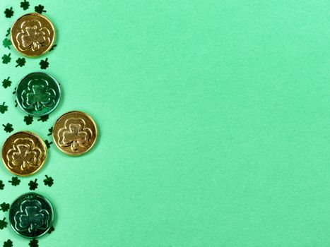 Saint Patricks Day with border of shamrocks and gold coins on green background with copy space 