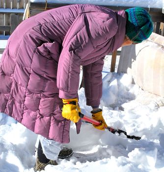 Mature female shoveling winter snow off patio deck outside.