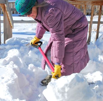 Mature female shoveling winter snow off patio deck outside.