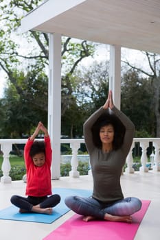 Mother and daughter meditating together in the porch at home