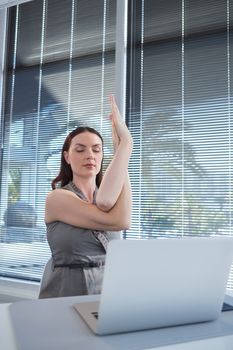 Female executive performing yoga at desk in office