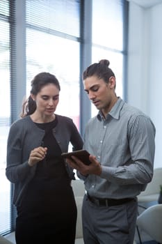 Colleagues discussing over digital tablet in waiting area of office