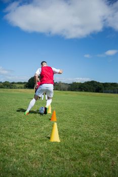 Soccer player dribbling through cones in the ground on a sunny day